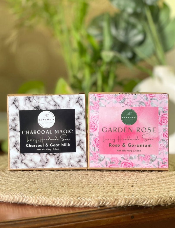 Two soap packages, one labeled 'Charcoal Magic' and the other 'Garden Rose', on a marble surface with decorative elements.