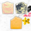 Three bars of soap with 'Raw Logic' branding on a marble surface with flowers.
