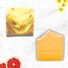 Two soap bars with 'Rawlogic' branding on a marble surface with grapefruit and flowers.