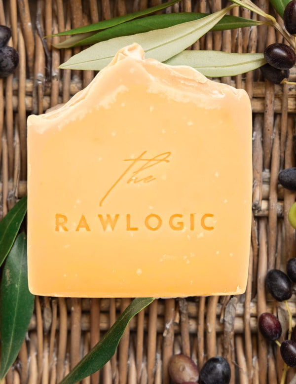 Bar of soap with 'the RAWLOGIC' branding on a woven background with leaves and olives.