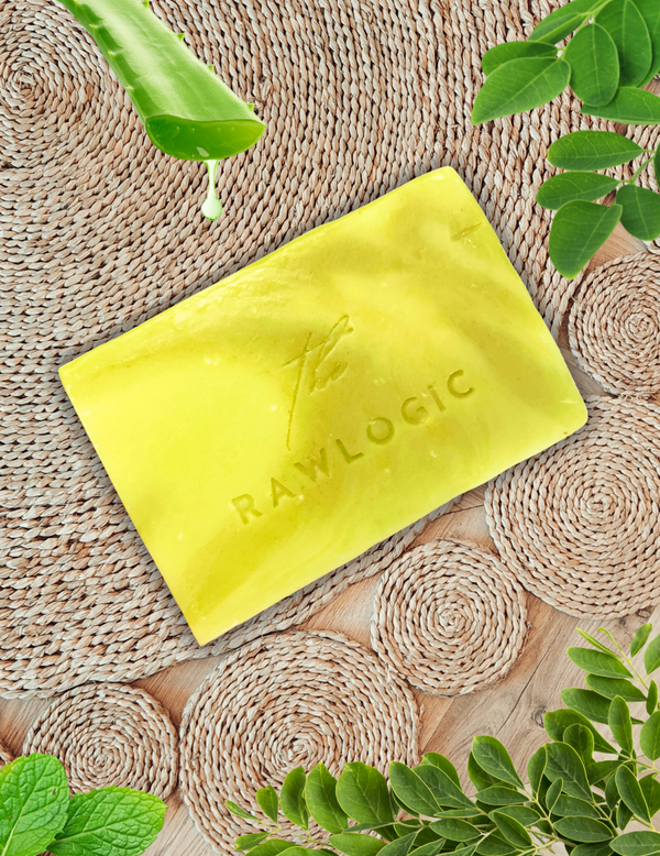 Yellow soap bar with 'RAWLOGIC' on a woven mat with green leaves.