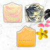 Three bars of soap with 'Raw Logic' branding on a marble surface with flowers.
